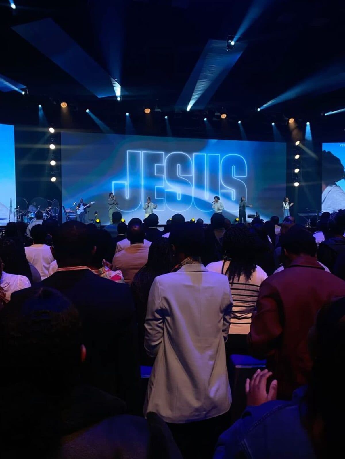 Congregação de pé durante o louvor, com a palavra JESUS projetada no telão do palco