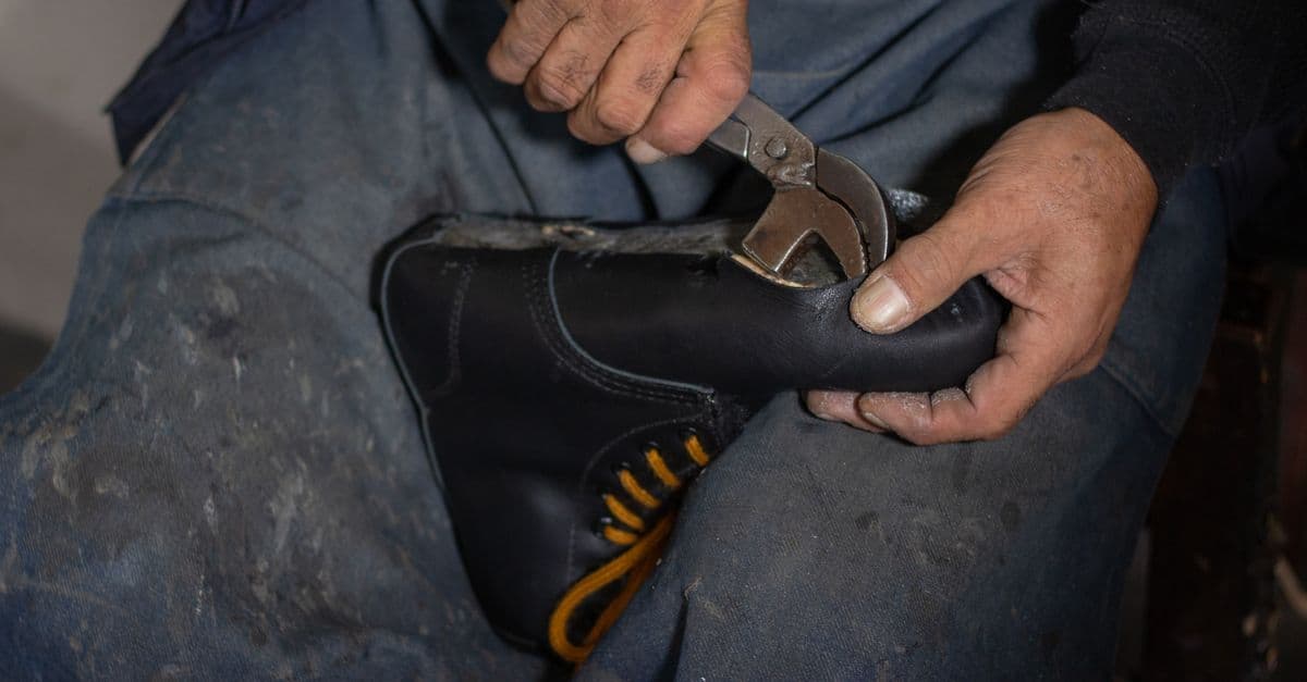 Um artesão habilidoso utiliza uma ferramenta para consertar um sapato de couro, demonstrando técnicas tradicionais de fabricação de calçados.